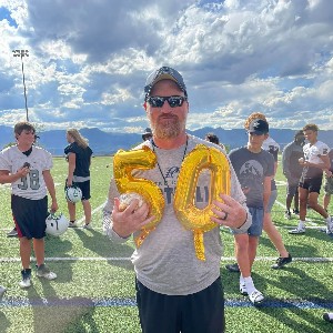 Todd Miller poses for a picture with a balloons signifying his 50th birthday surrounded by his football players